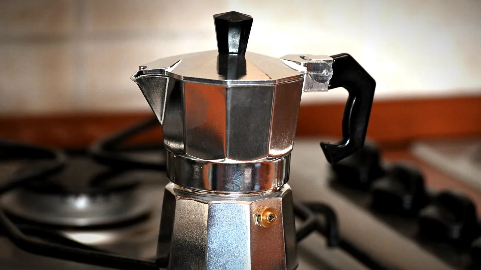 An aluminum stovetop moka pot sitting on a gas stove grate