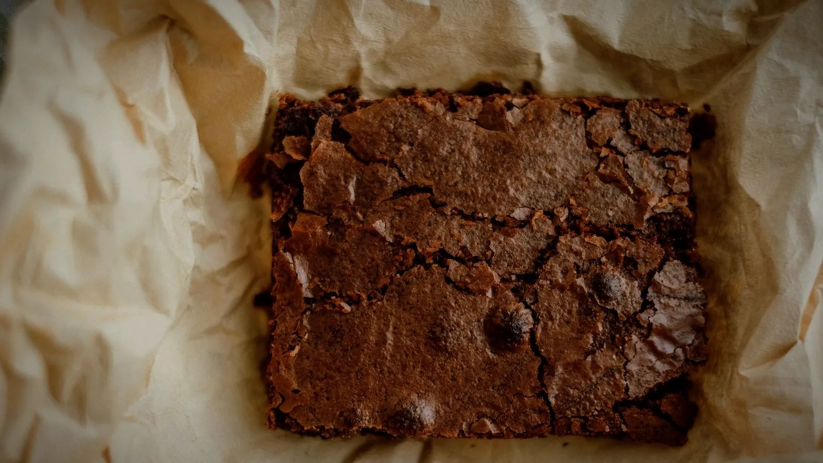 A freshly baked slab of chocolate brownie on crumpled parchment paper