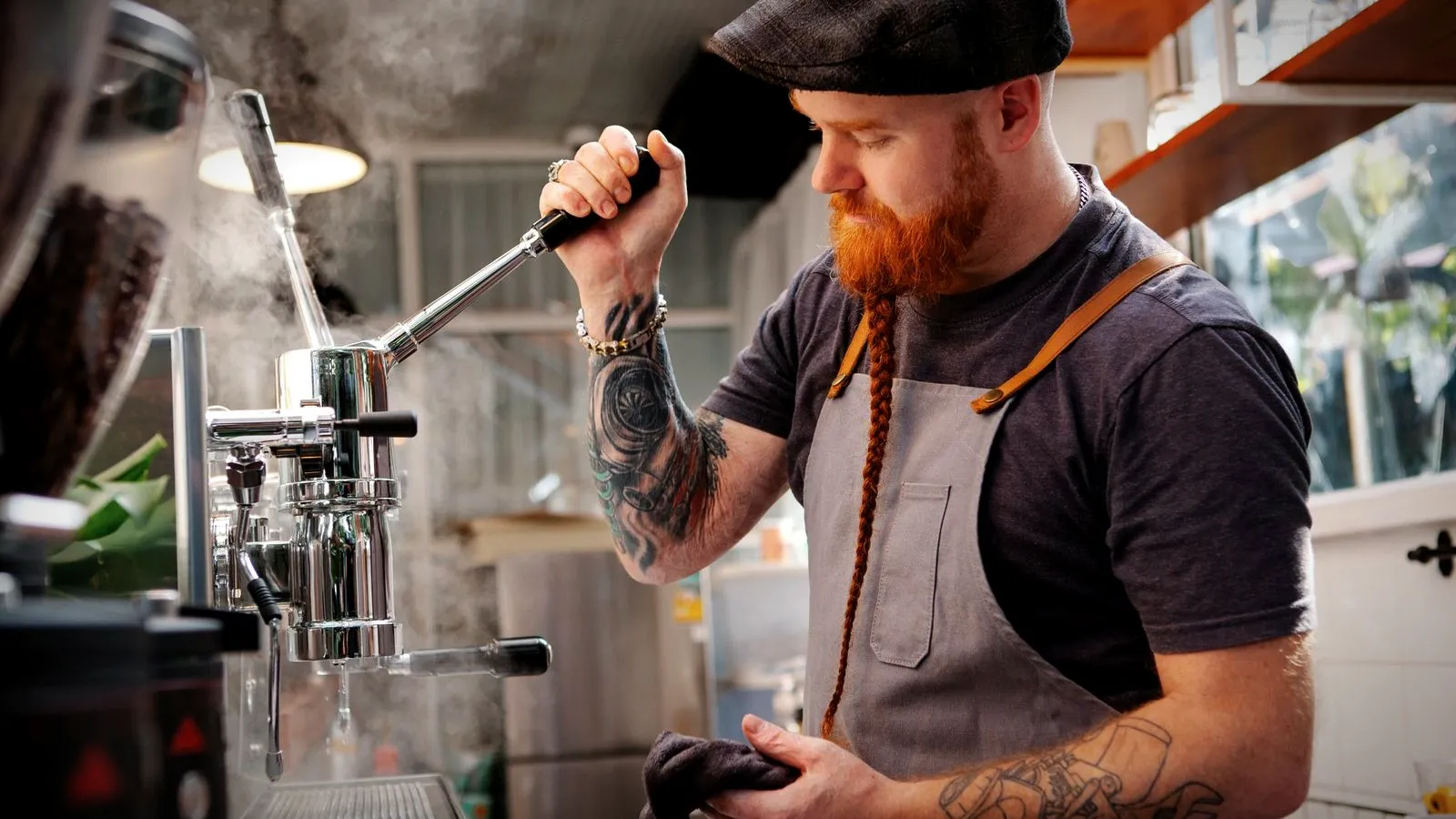A barista pulling down the lever of a chrome lever espresso machine