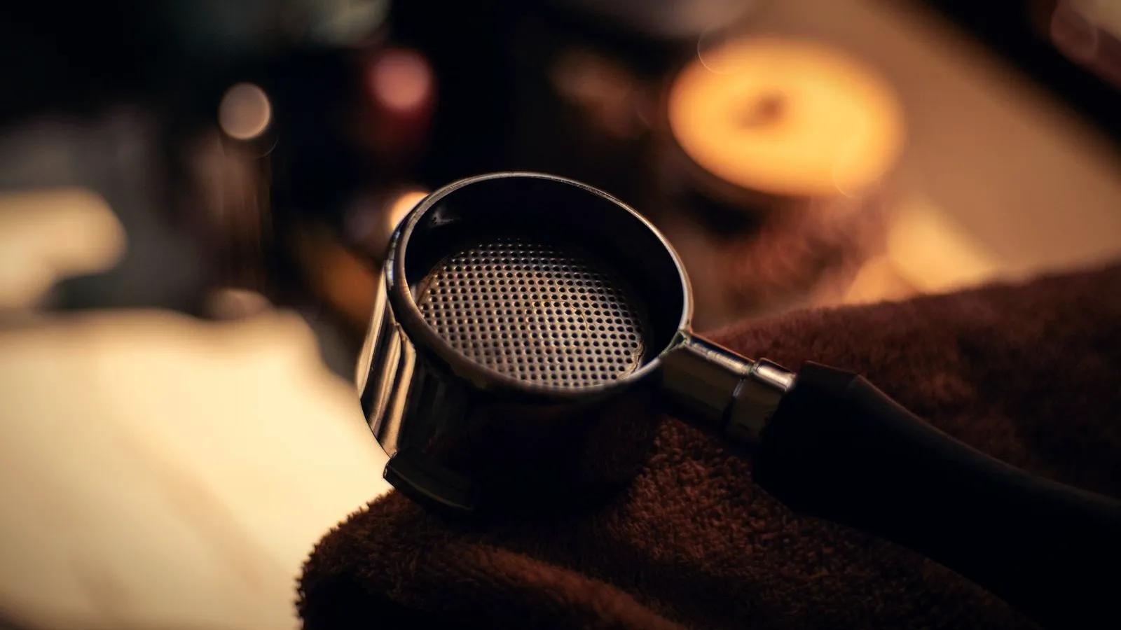 An empty portafilter basket with its fine perforated floor, resting on a dark towel