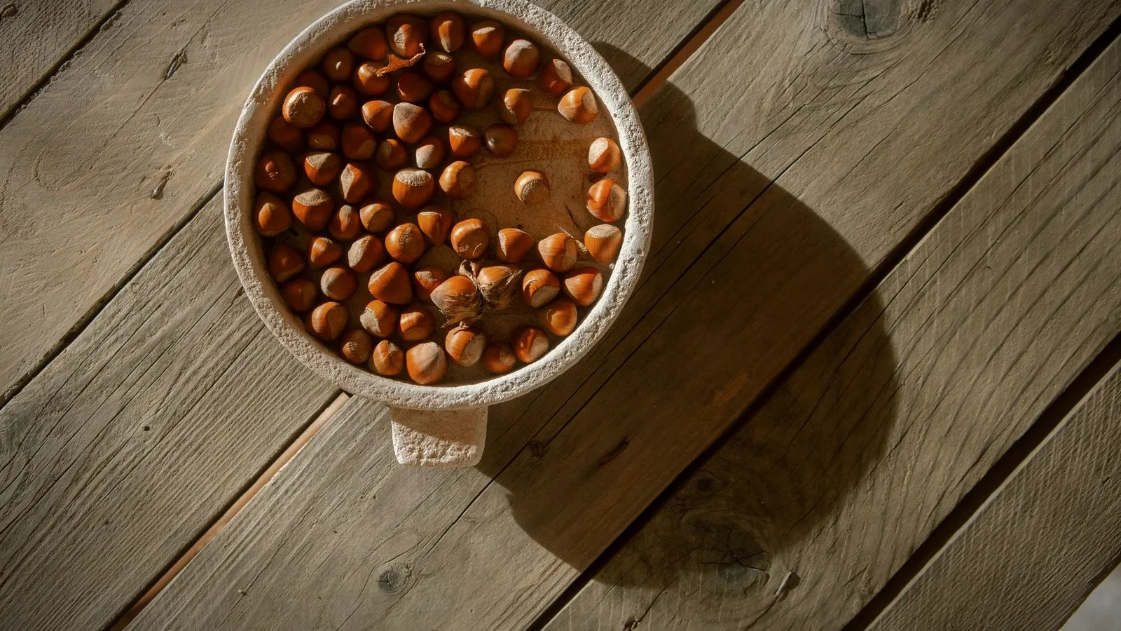 A bowl of whole hazelnuts on a weathered wooden table