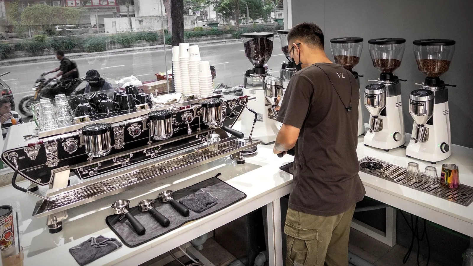 Barista working at a café espresso bar with a multi-group commercial espresso machine and a row of grinders
