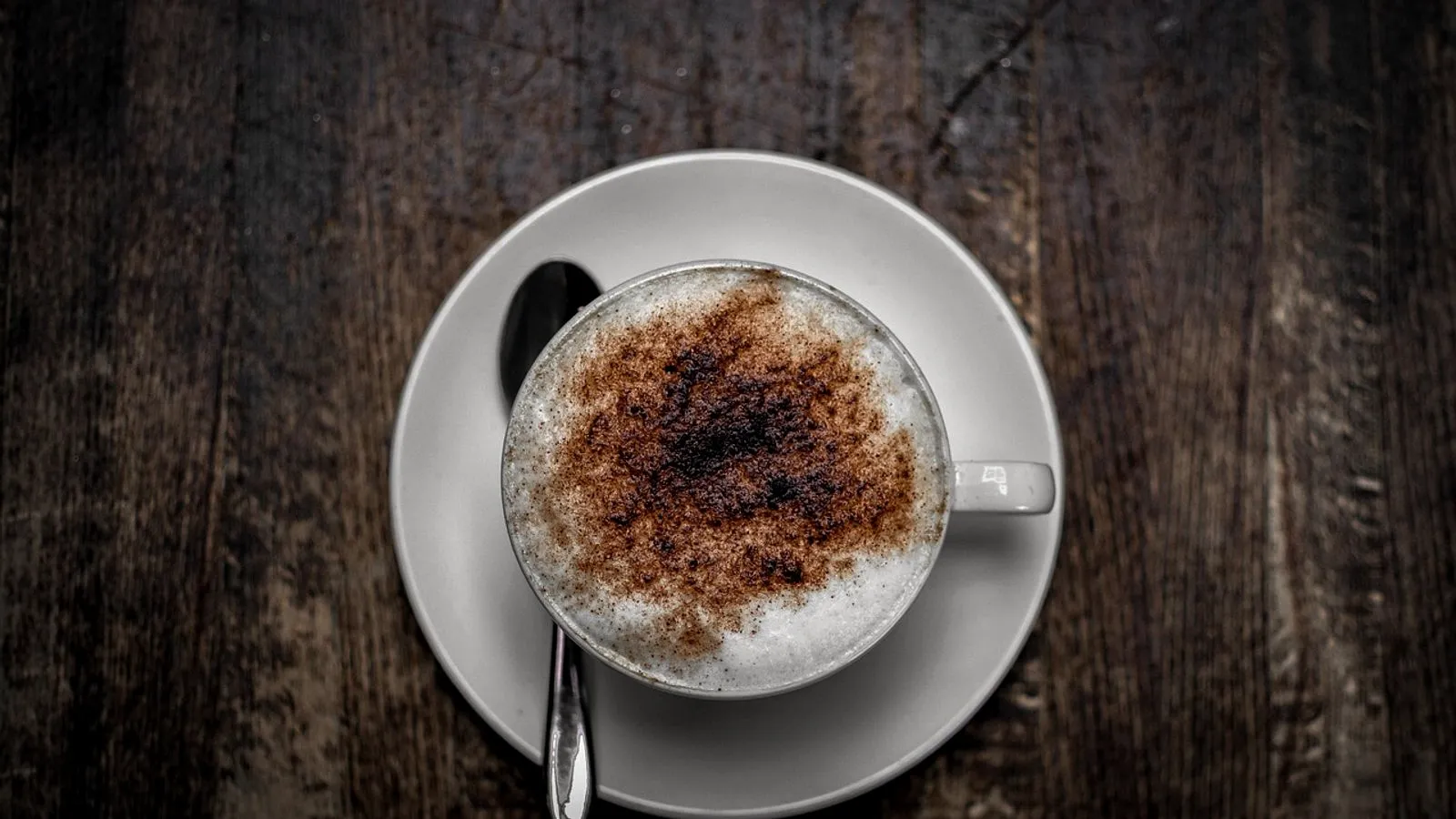 A cappuccino dusted with cocoa in a white cup and saucer, seen from above