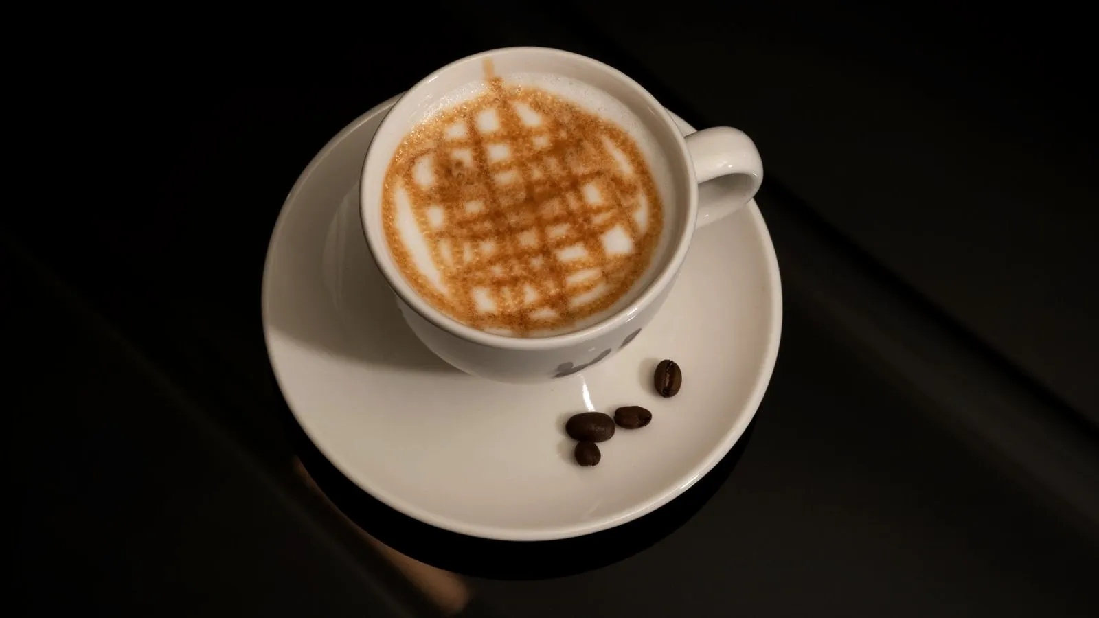 Cup of milky coffee with a crosshatch of caramel drizzle on the foam, coffee beans on the saucer