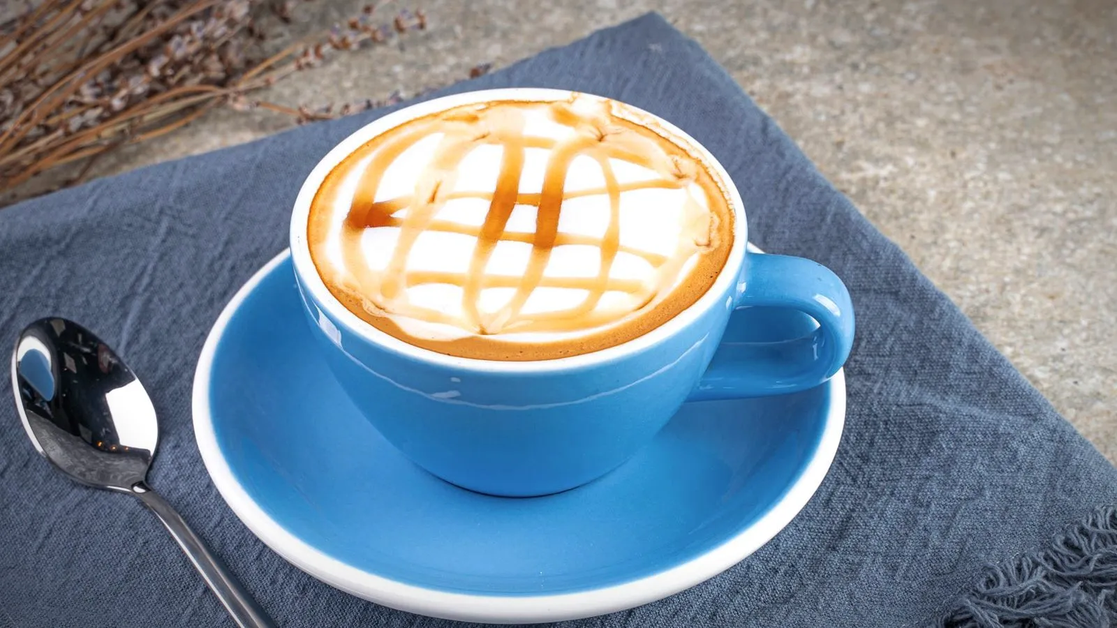 Latte topped with a caramel sauce drizzle in a blue cup and saucer with a spoon