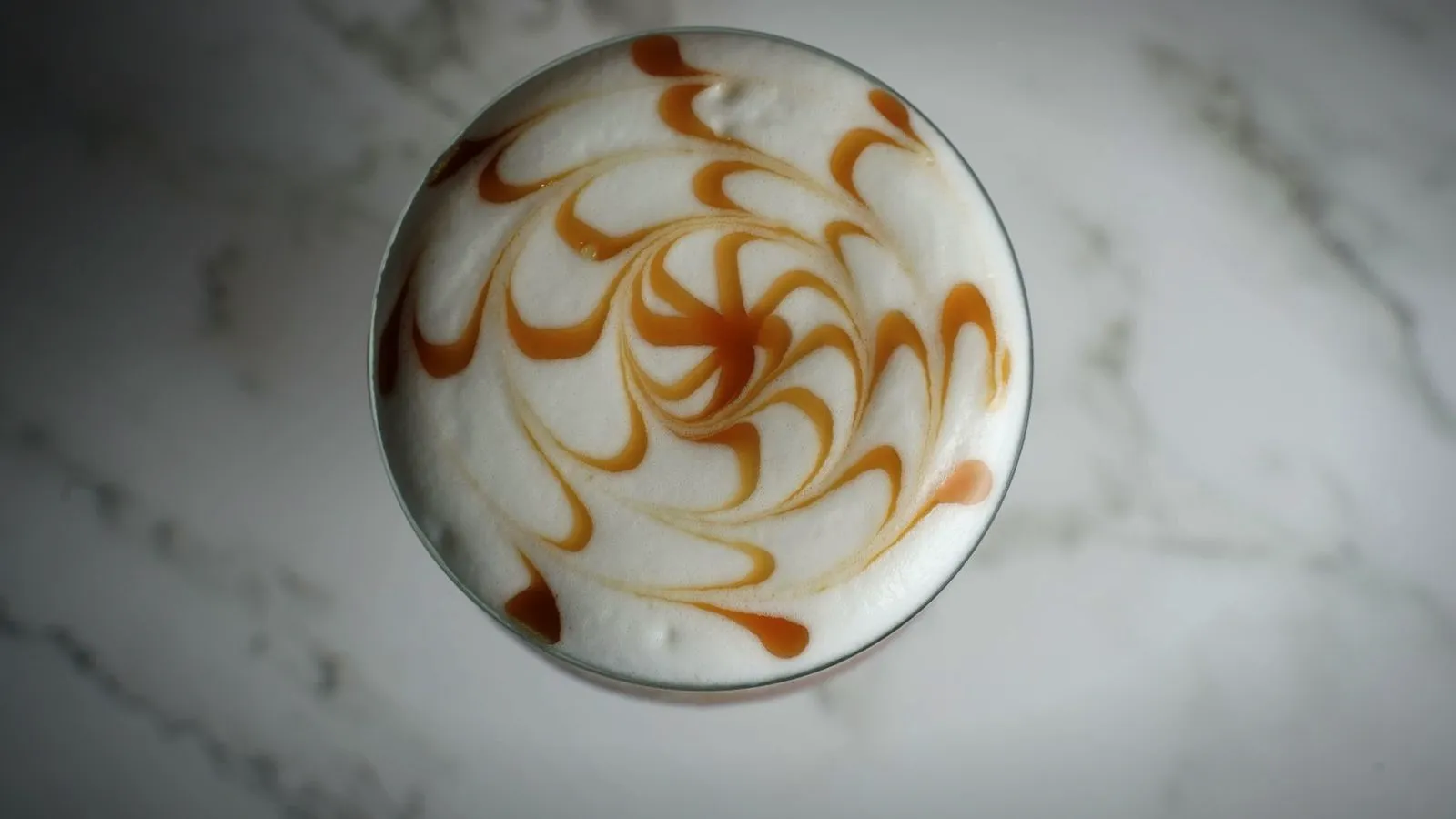Top view of a milk coffee with a spiral of caramel drizzled over the foam