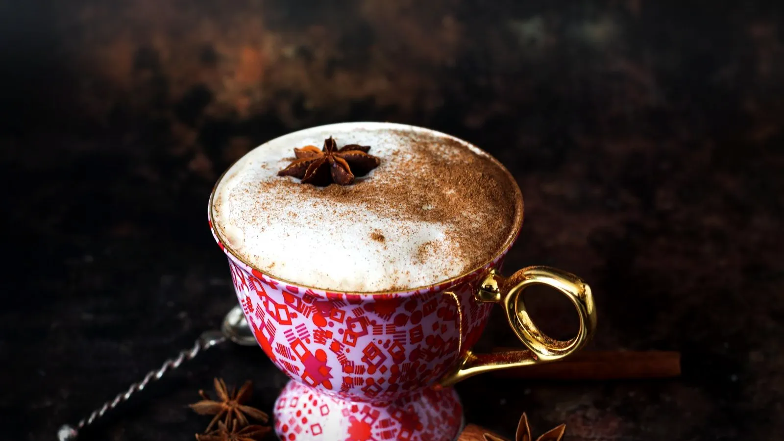 A spiced milky latte dusted with cinnamon and topped with a star anise in a patterned teacup, with cinnamon sticks nearby