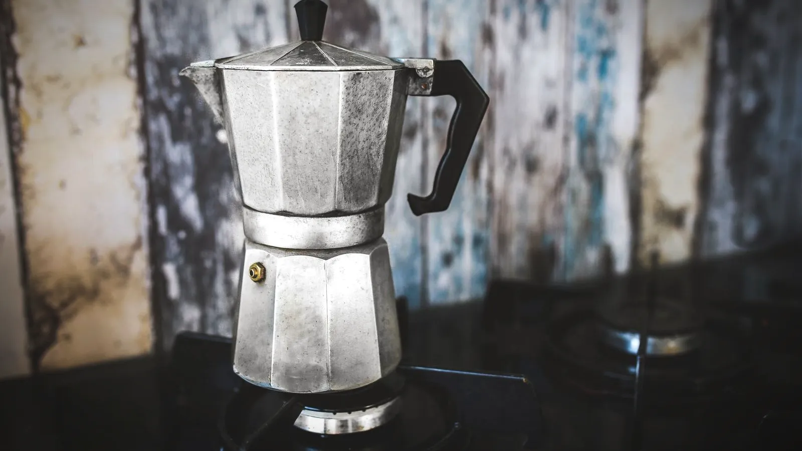 Classic eight-sided aluminum moka pot on a gas stove against weathered wood