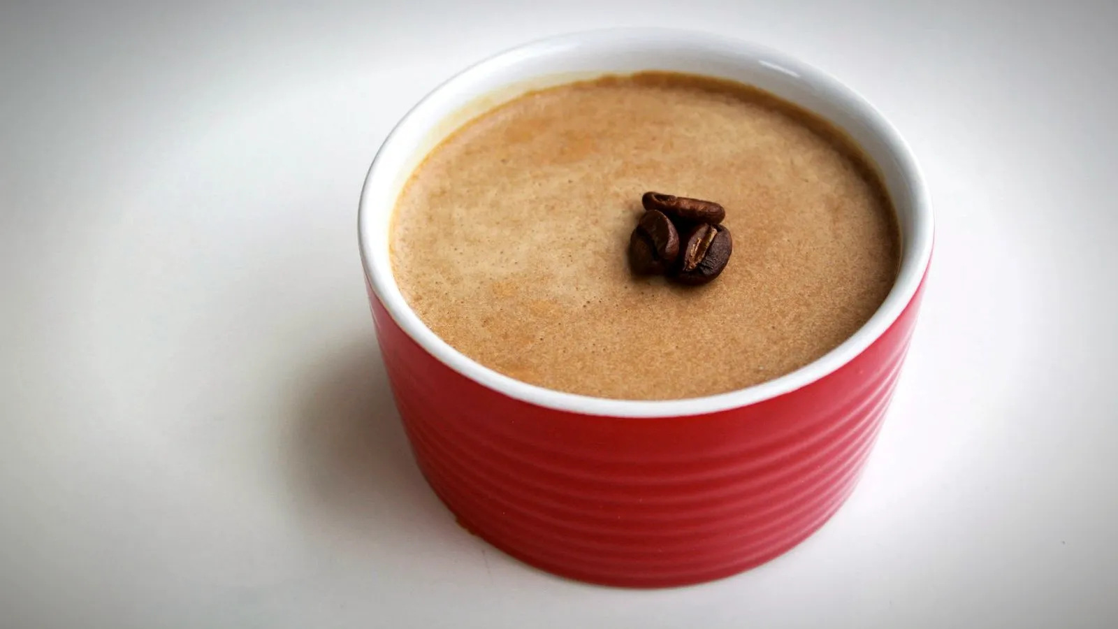 Coffee cream dessert in a red ramekin topped with three roasted coffee beans