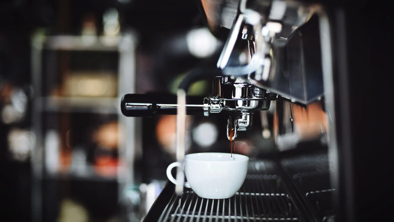 Espresso pouring from the portafilter of a commercial machine into a white cup