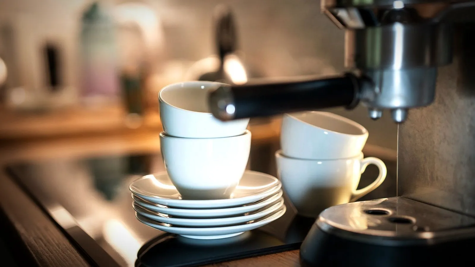 White cups and saucers stacked beside a compact home espresso machine with its portafilter in place