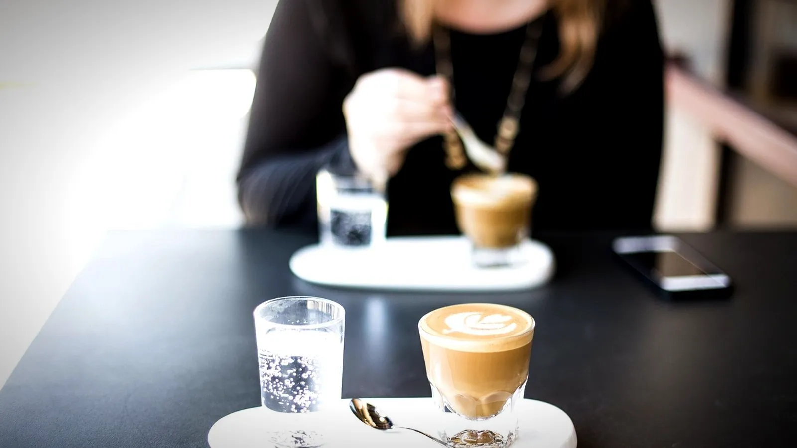 A small cortado in a glass served on a tray with a glass of water