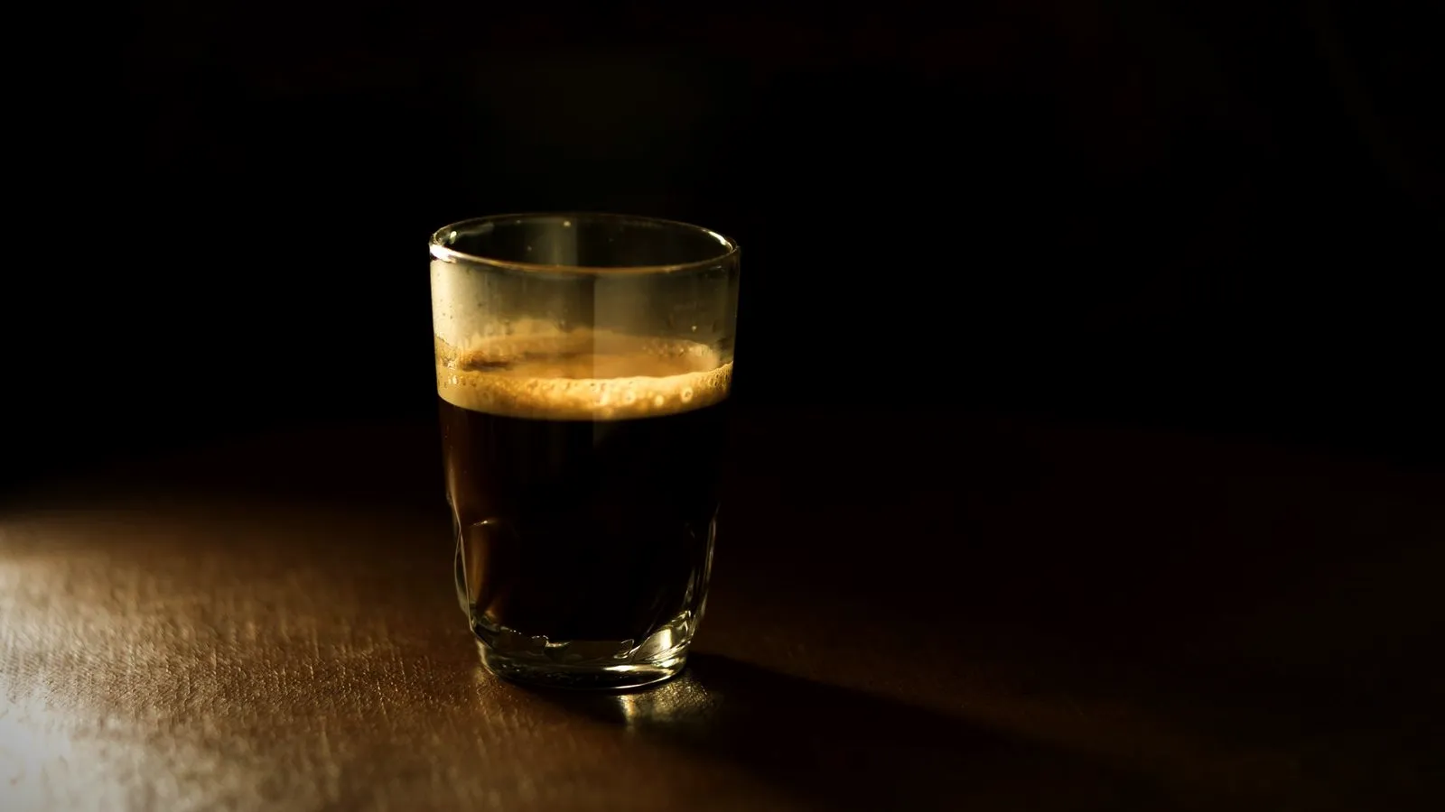 Dark espresso shot in a small glass on a wooden counter in low light
