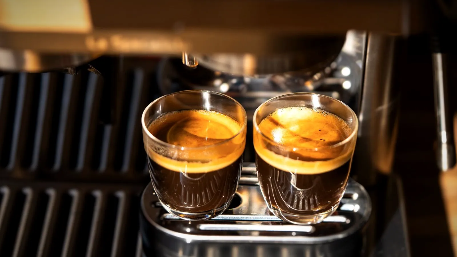 Two freshly pulled espresso shots in small glasses on an espresso machine drip tray
