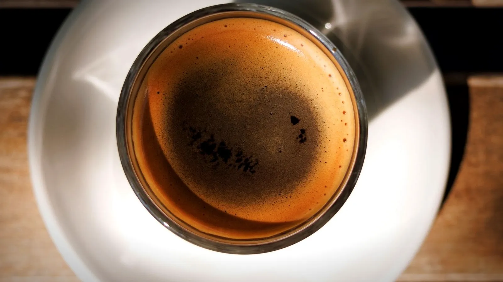 Espresso in a glass cup seen from above, the crema dark in the center with a few black specks