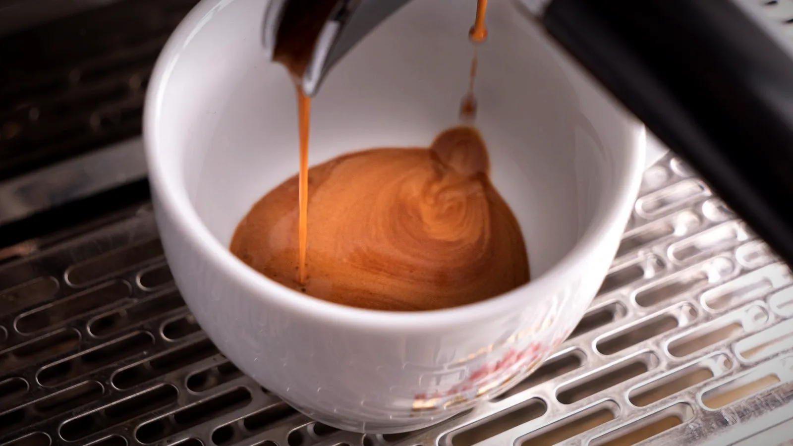Espresso flowing from a portafilter spout into a white cup, crema swirling on the surface