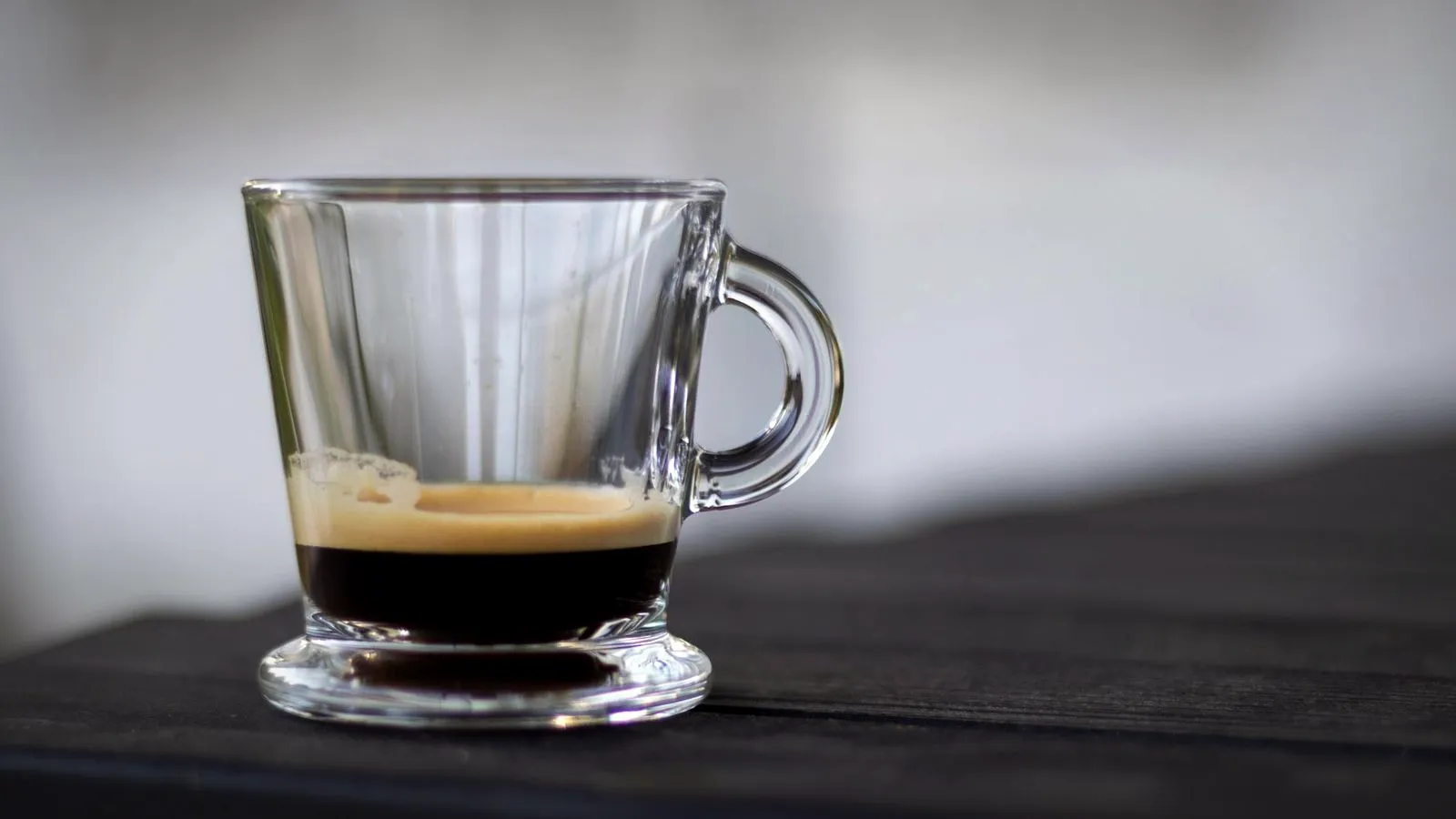 Short espresso with a thin layer of crema in a clear glass cup on a dark wooden table