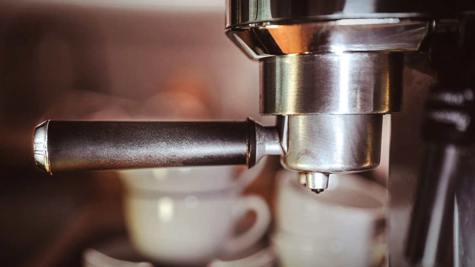An espresso machine portafilter locked into the group head above stacked white cups