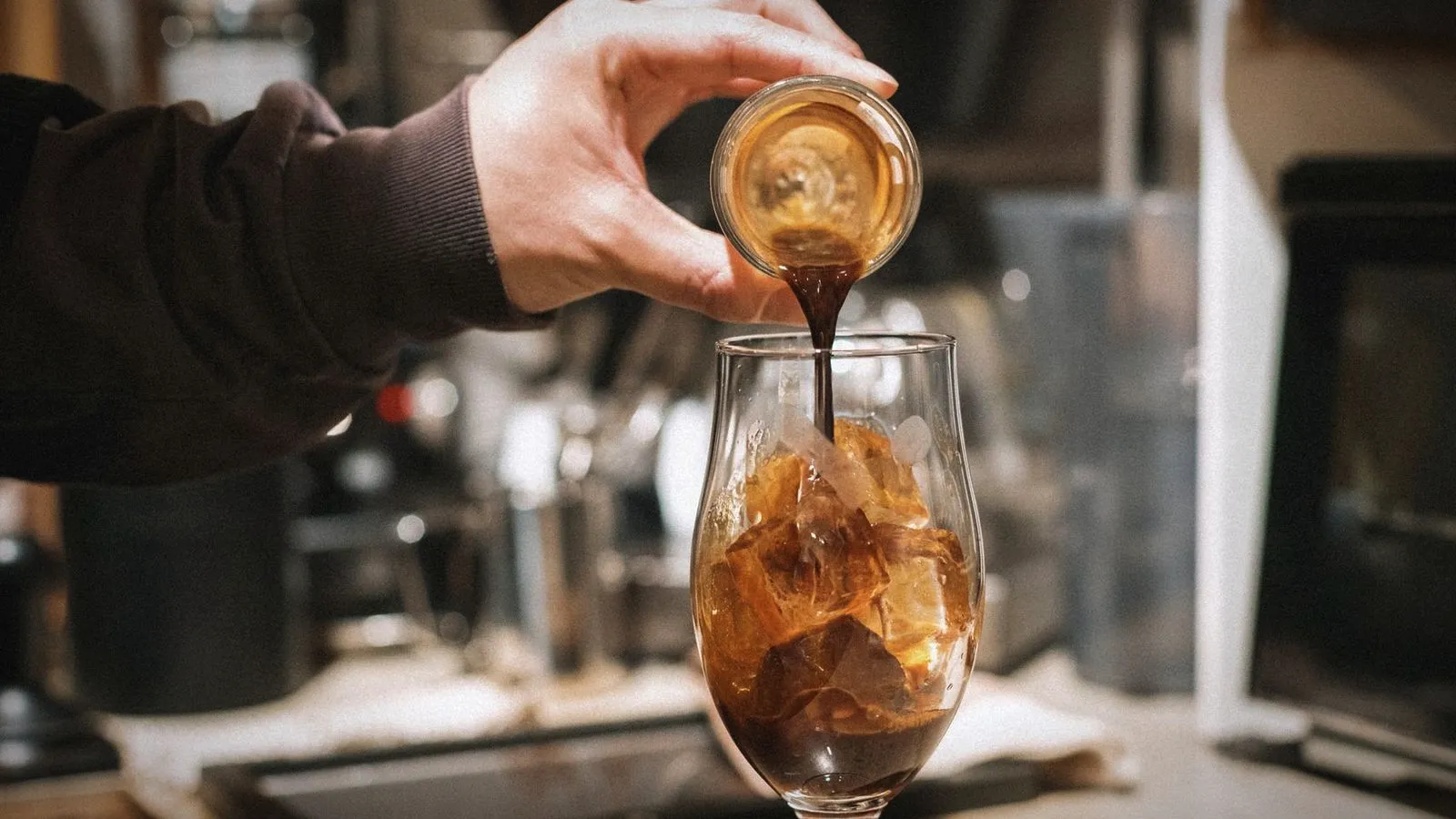 Espresso poured from a small glass into a stemmed glass filled with ice and coffee
