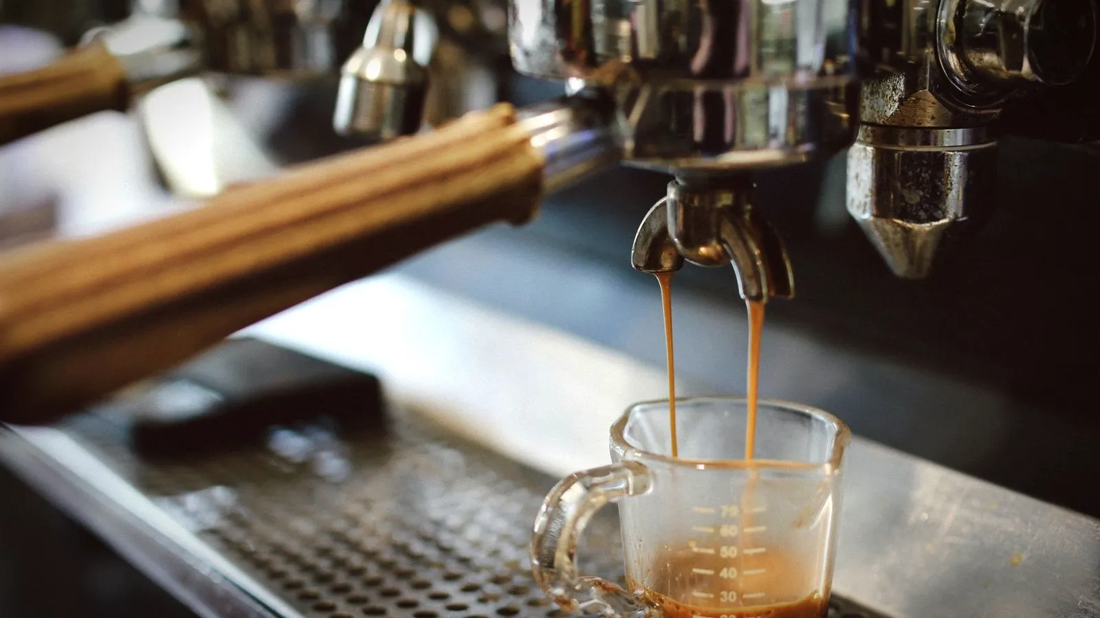 Espresso pouring from a double spout into a measuring shot glass on the drip tray