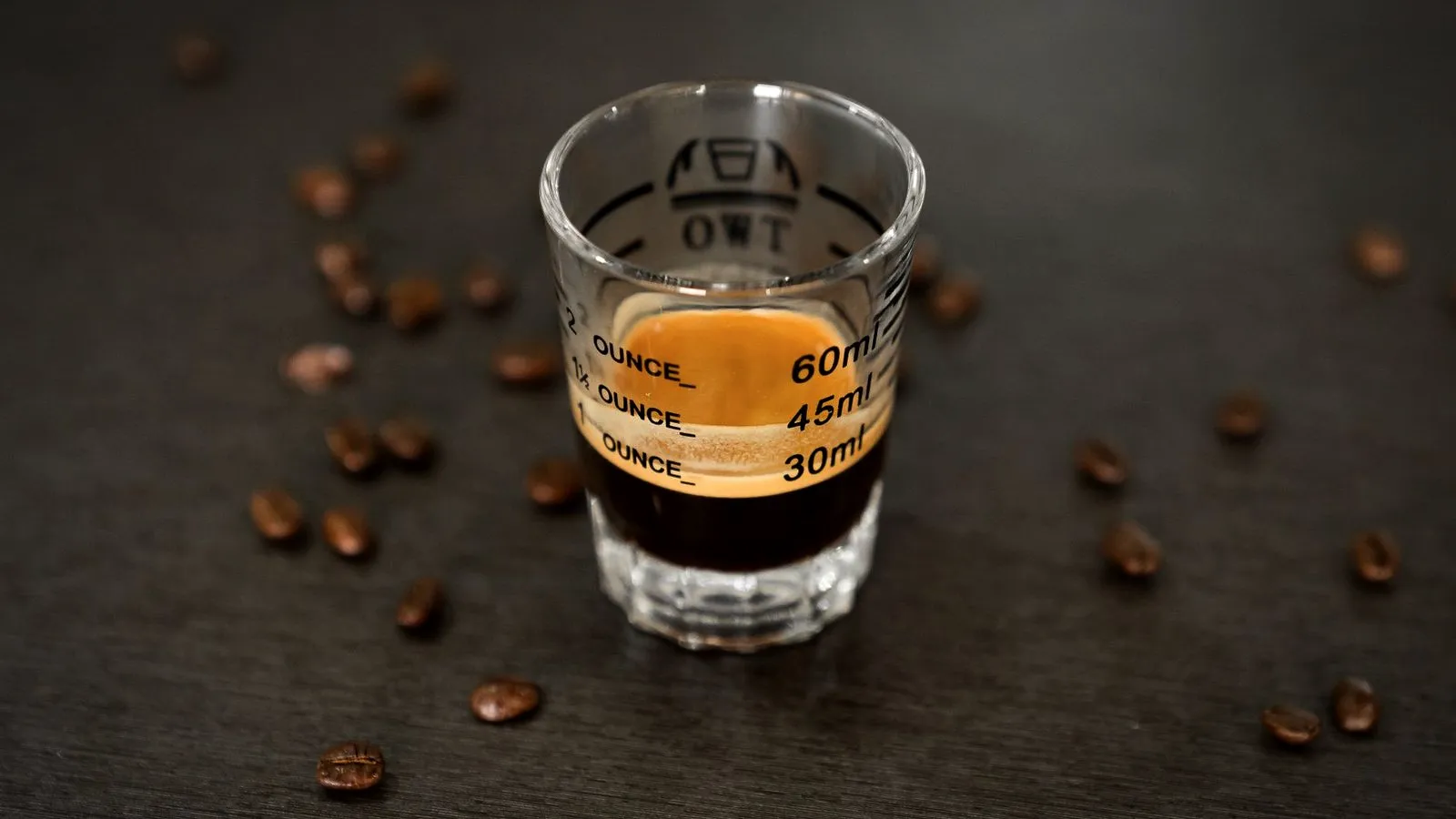 A double espresso shot in a measuring glass surrounded by roasted coffee beans