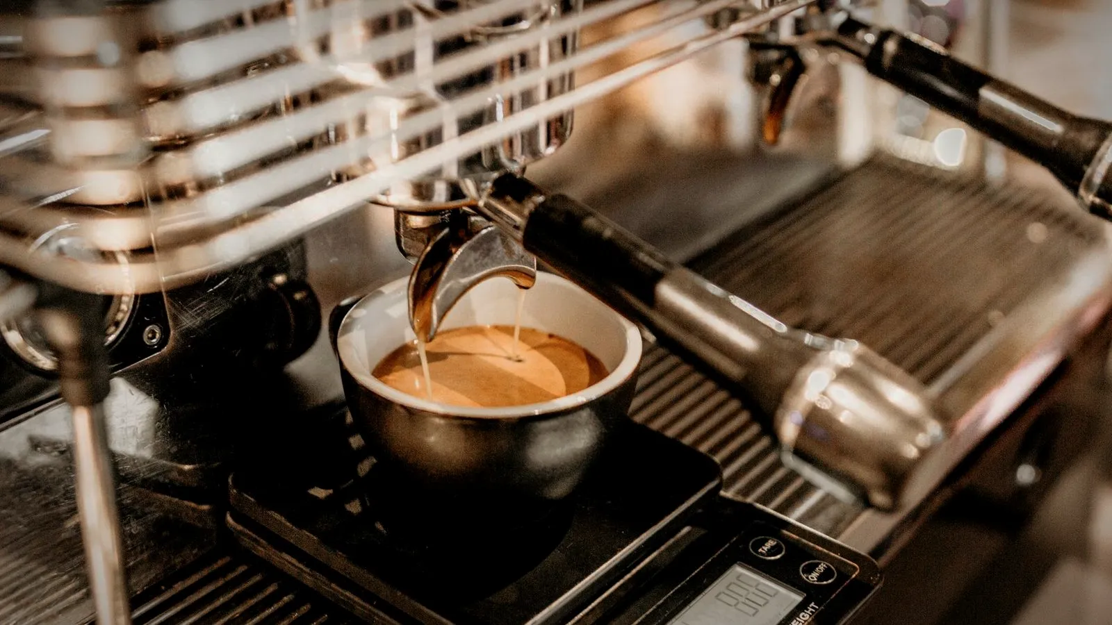 Espresso pouring from a portafilter into a cup that sits on a digital scale on the drip tray