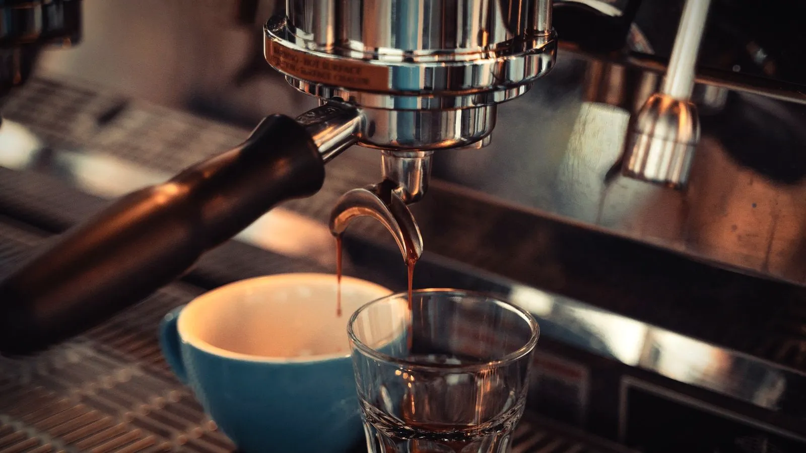 Espresso pouring from a portafilter into a small glass under an espresso machine