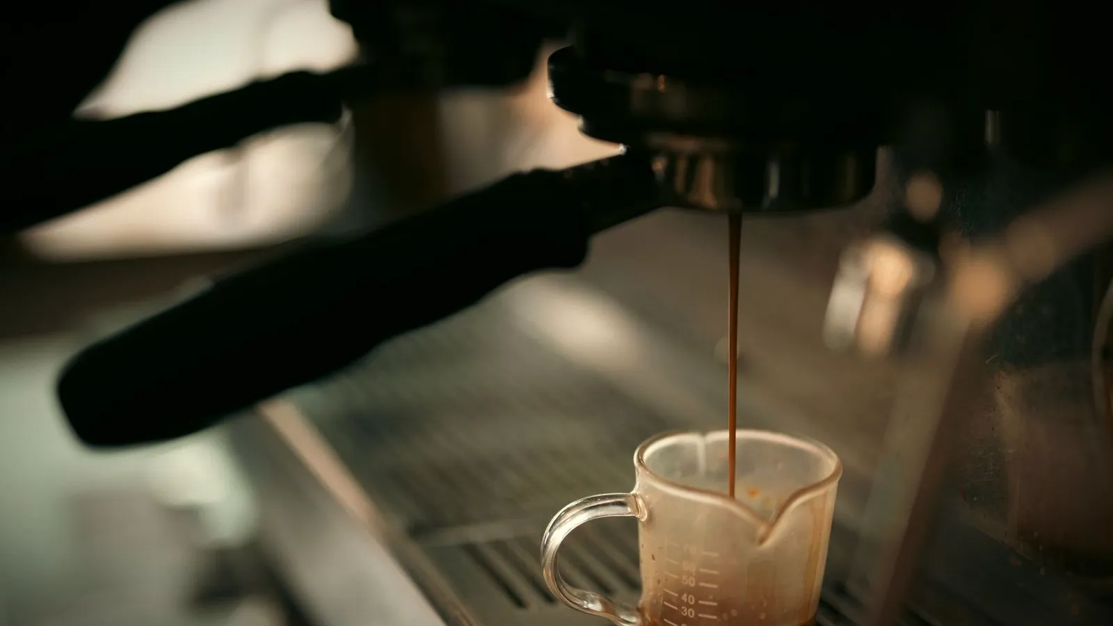 Thin stream of espresso running from a portafilter into a small glass jug on the drip tray