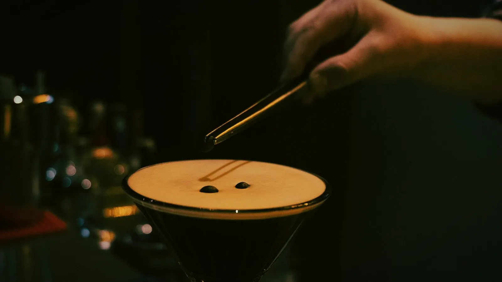 A bartender placing coffee beans on the foam of an espresso martini with tweezers