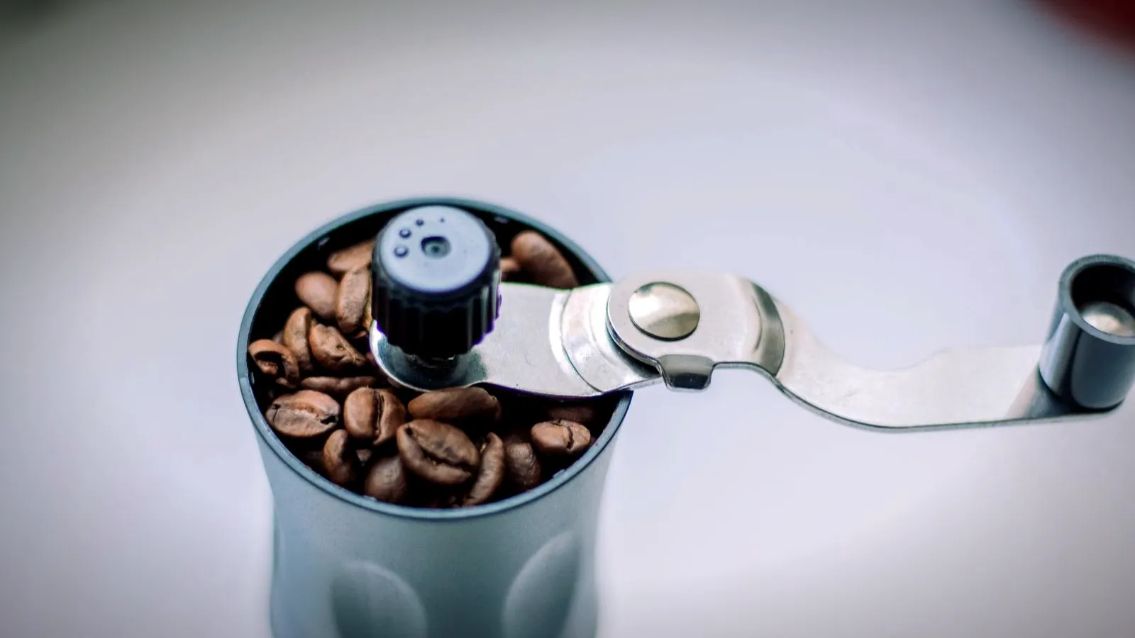 A hand-crank coffee grinder filled with roasted coffee beans