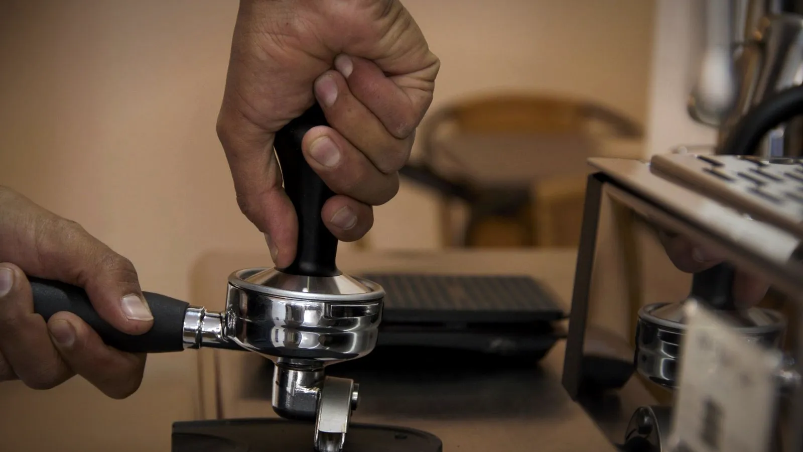 Side view of a hand pressing a tamper straight down into a portafilter resting on a rubber tamping mat