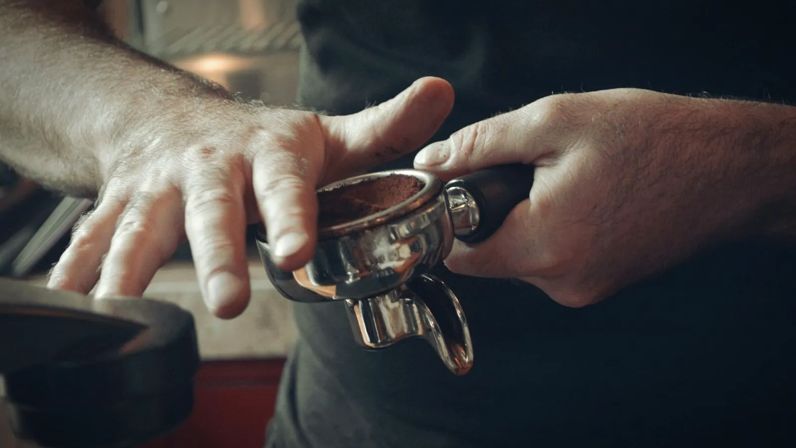 Hands holding a double-spout portafilter filled with ground coffee