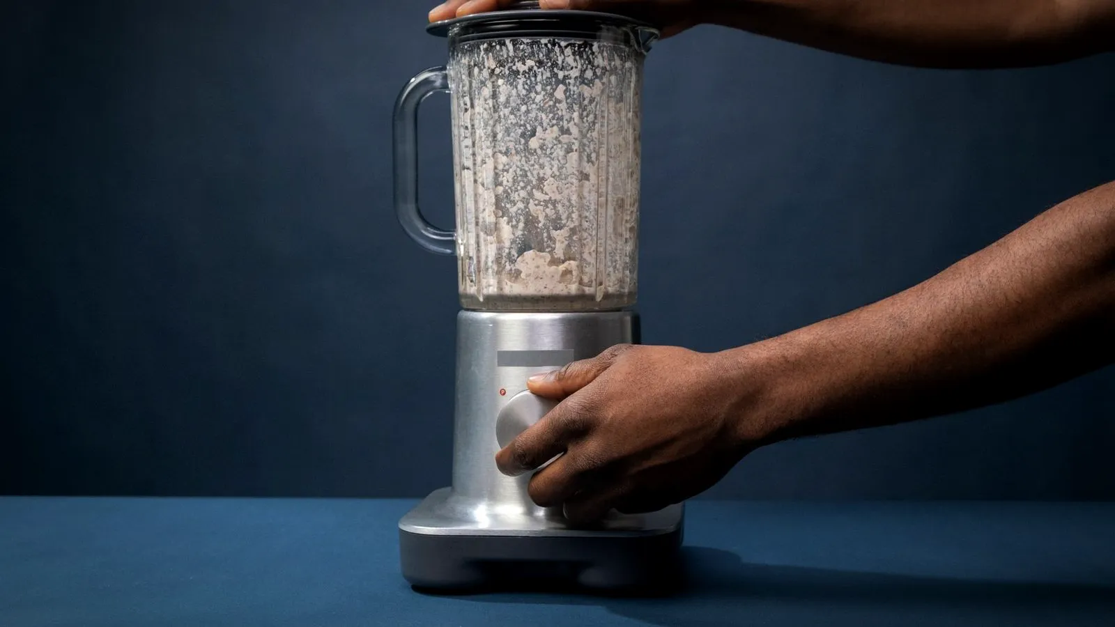 Hands holding a blender lid down and turning the dial while it blends a light brown drink