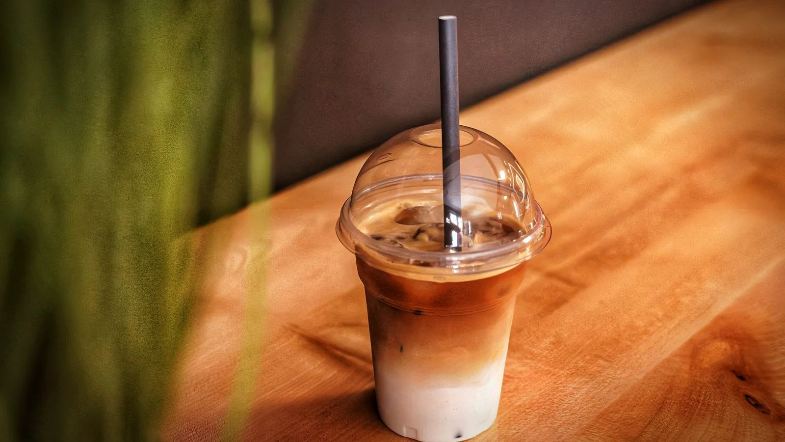An iced latte in a clear cup with a straw on a wooden counter, milk and espresso still layered