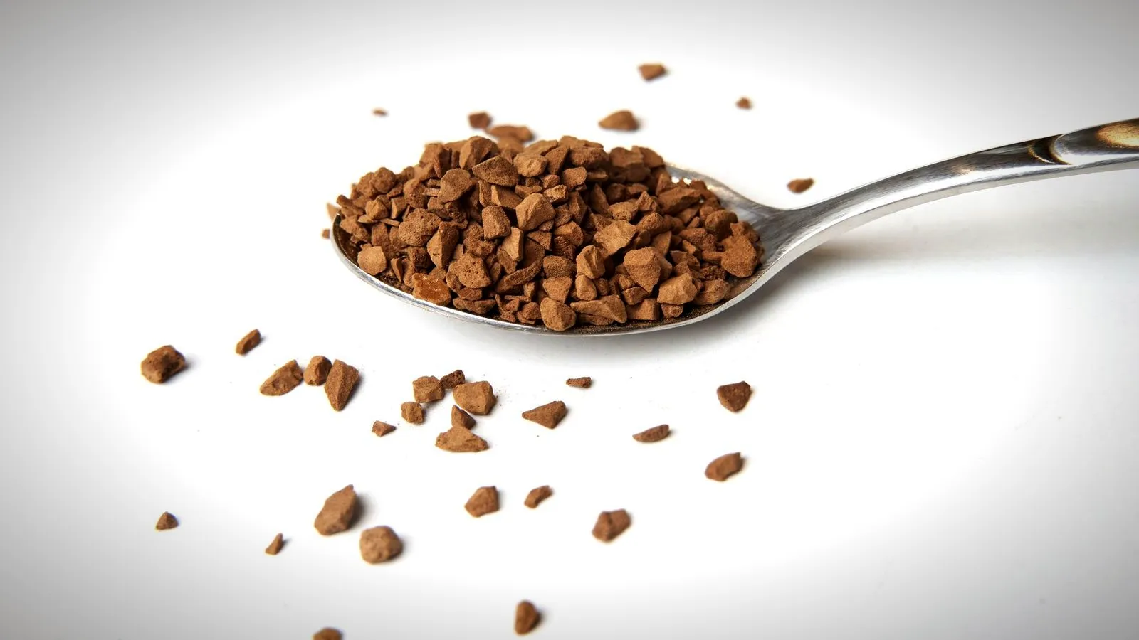 Freeze-dried instant coffee granules in a teaspoon on a white background