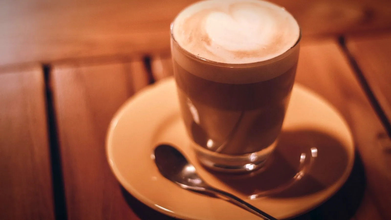 Side view of a latte in a glass on a saucer, with espresso and milk below a thin layer of foam