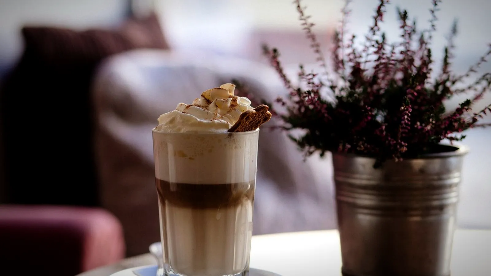 A layered espresso and milk drink in a tall glass topped with cream