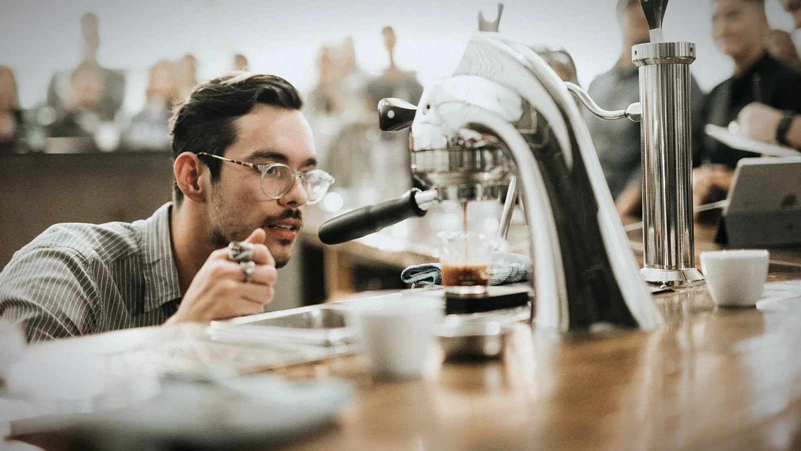 A man watching a shot pull from a chrome lever espresso press on a café counter
