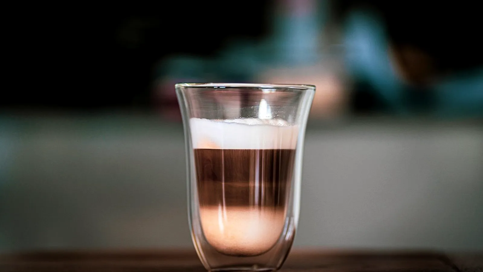 A layered milk and espresso drink in a clear double-walled glass on a wooden table