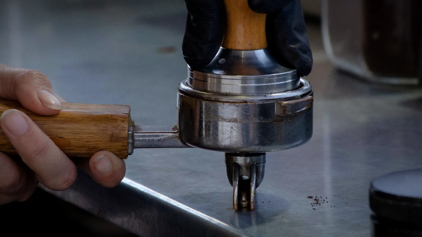 Gloved hand pressing a palm-style distribution tool onto a portafilter basket
