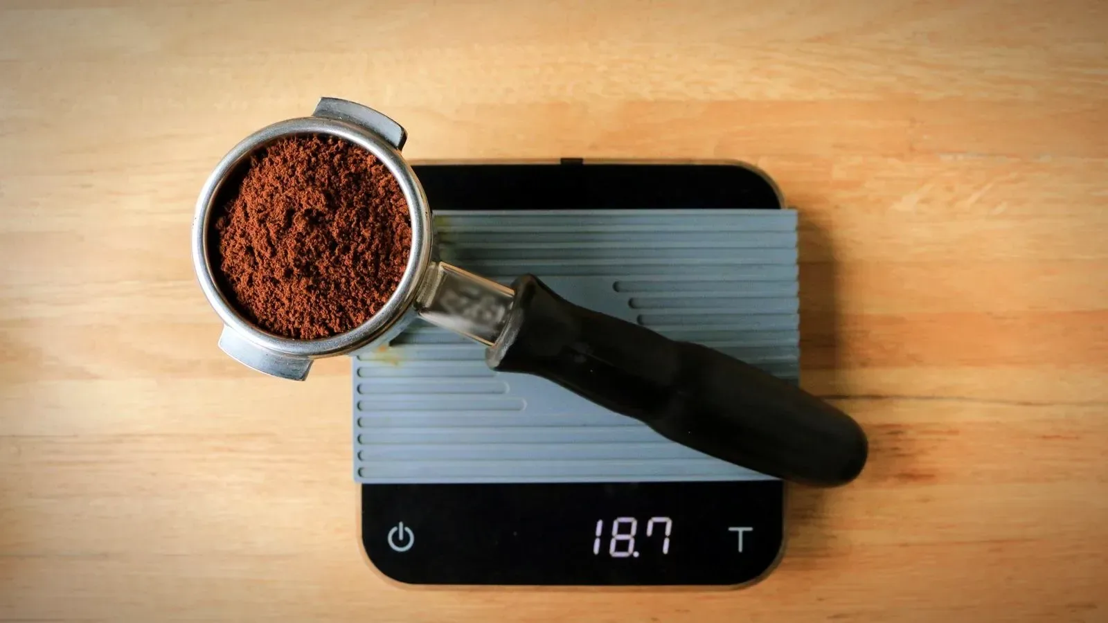Top view of a portafilter filled with ground coffee resting on a digital scale on a wooden table