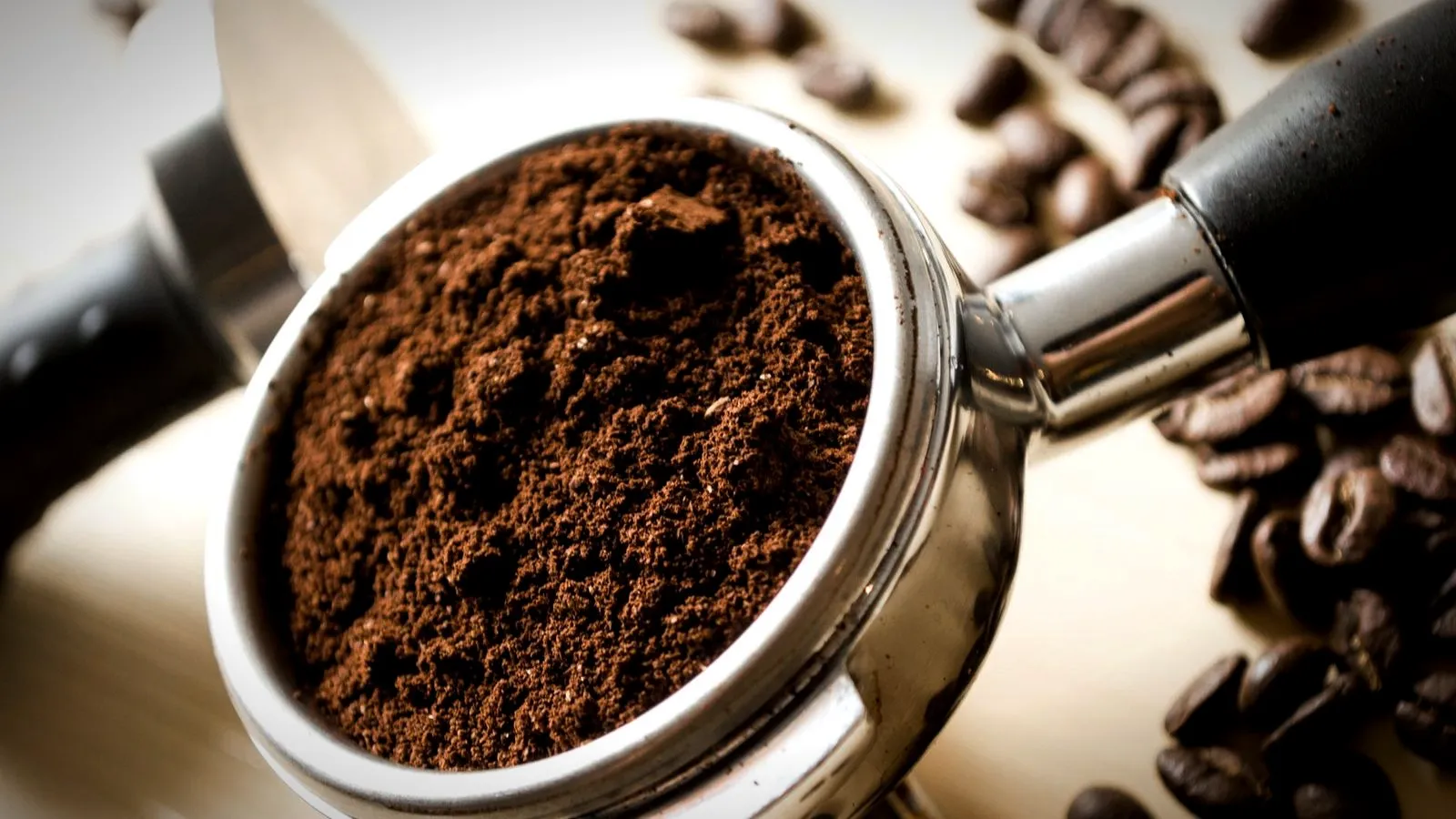 Portafilter basket heaped with fine espresso grounds, whole coffee beans beside it