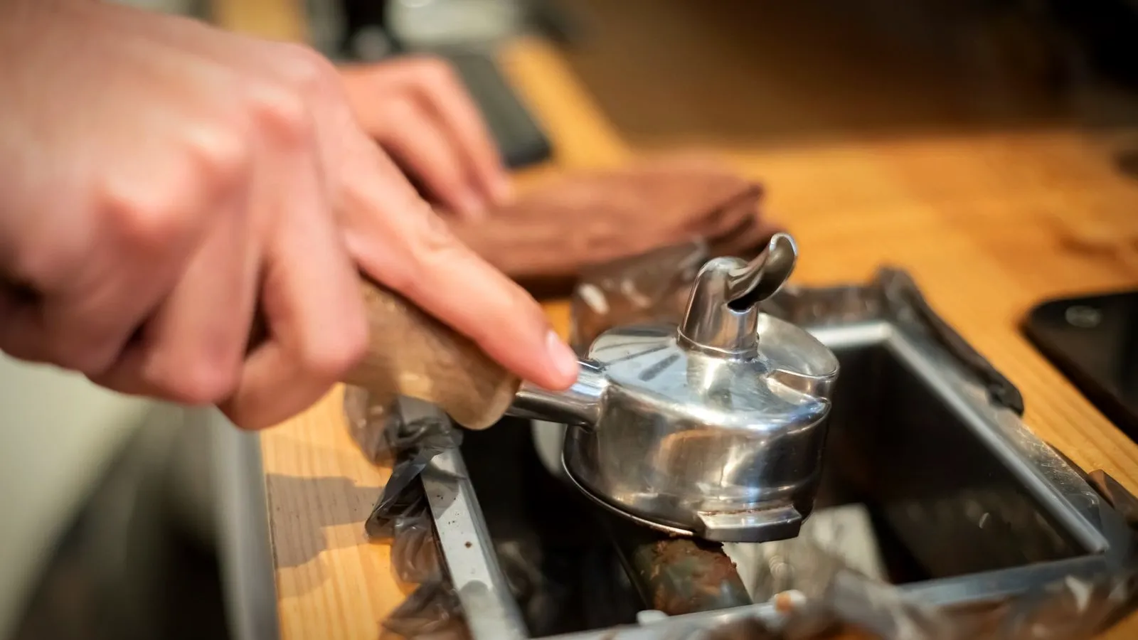 Hand knocking an upside-down portafilter against the bar of a knock box, with a towel on the counter behind