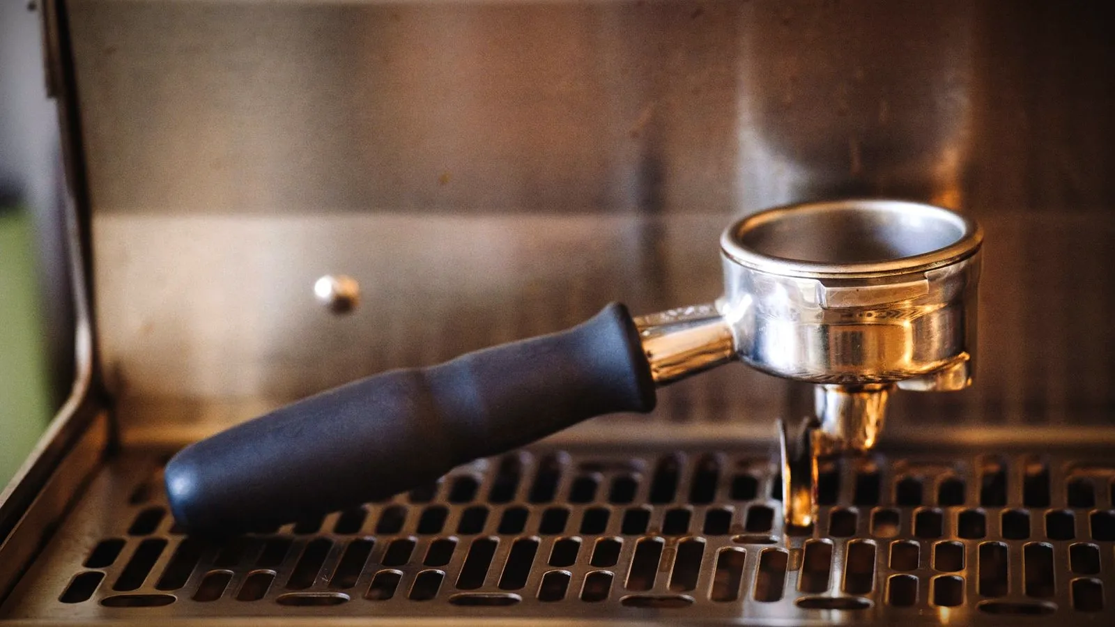 An empty spouted portafilter resting on the stainless drip tray of an espresso machine