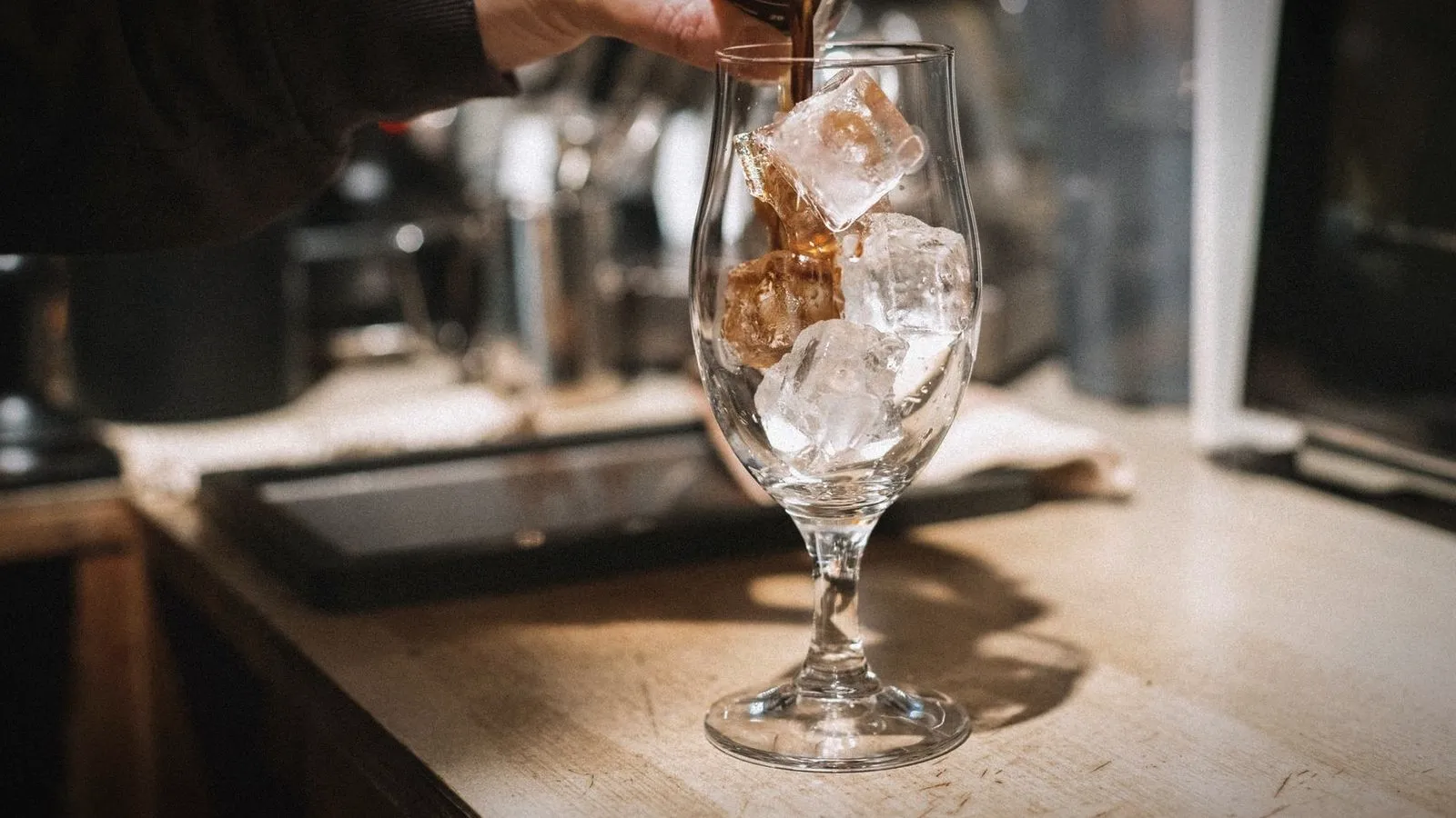 Espresso being poured over ice cubes in a stemmed glass on a coffee bar counter