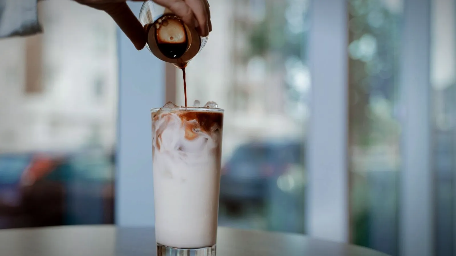 Espresso being poured from a small pitcher into a glass of iced milk