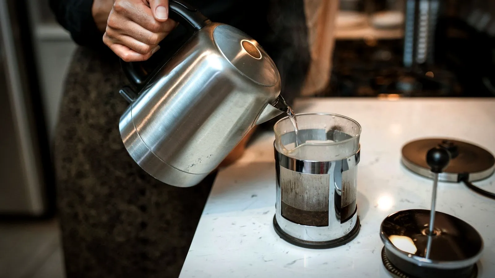 Pouring hot water from a kettle into a French press on a kitchen counter