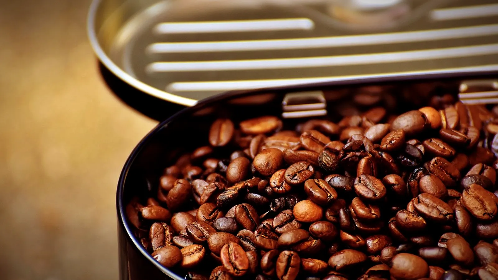 Roasted coffee beans inside an opaque metal storage tin with the lid lifted