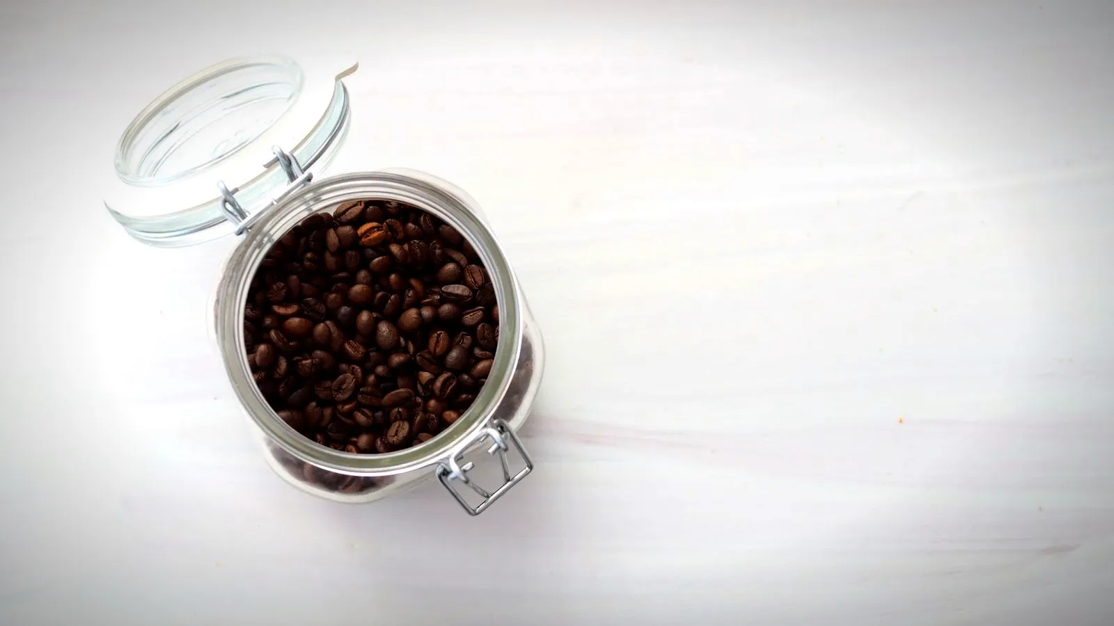 Roasted coffee beans in a clip-top glass jar on a white table
