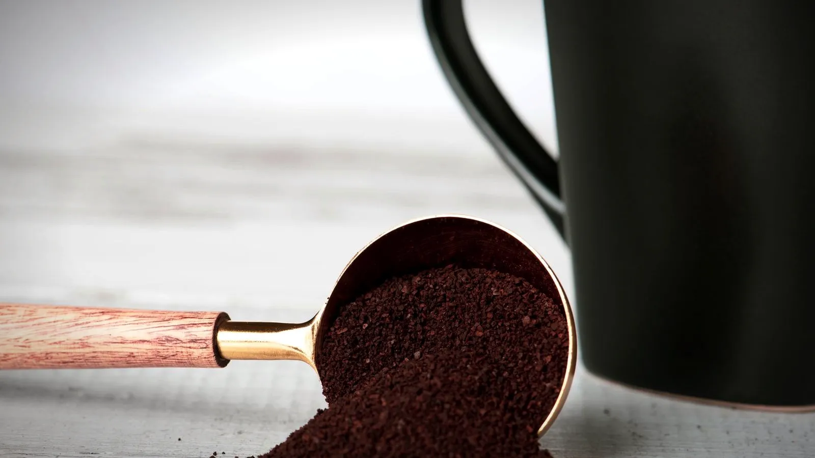 Fine ground coffee spilling from a copper measuring scoop onto a table